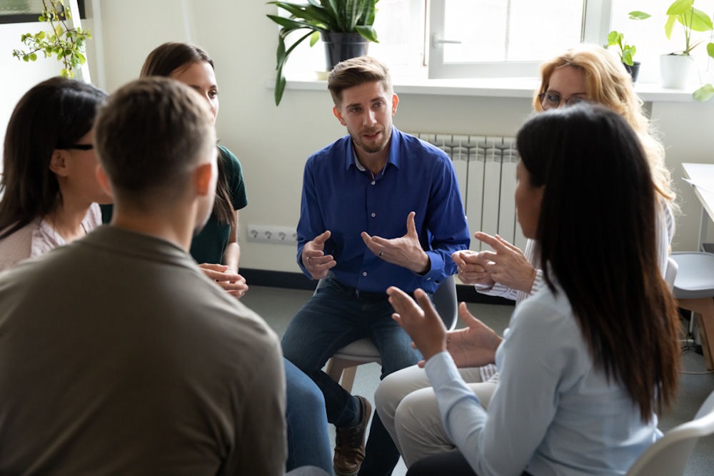 a man in blue shirt talking to patients sitting in circle