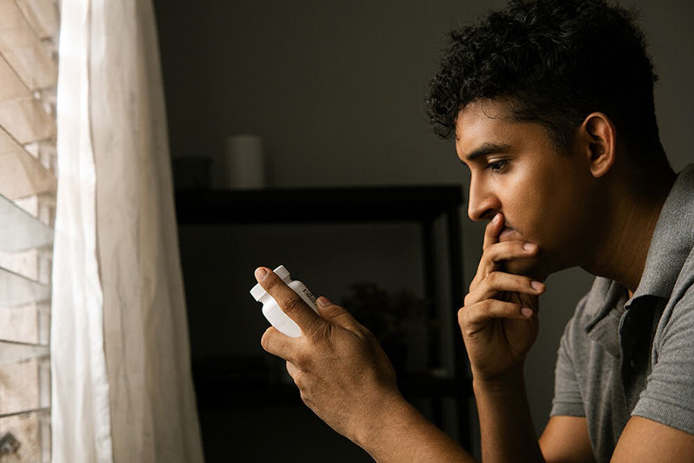 Man holding a pill bottle, reflecting on peer pressure and substance abuse.