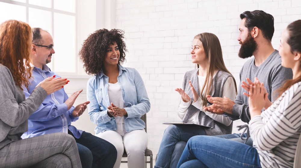 Support group applauding a member during a session on bipolar disorder and substance abuse recovery