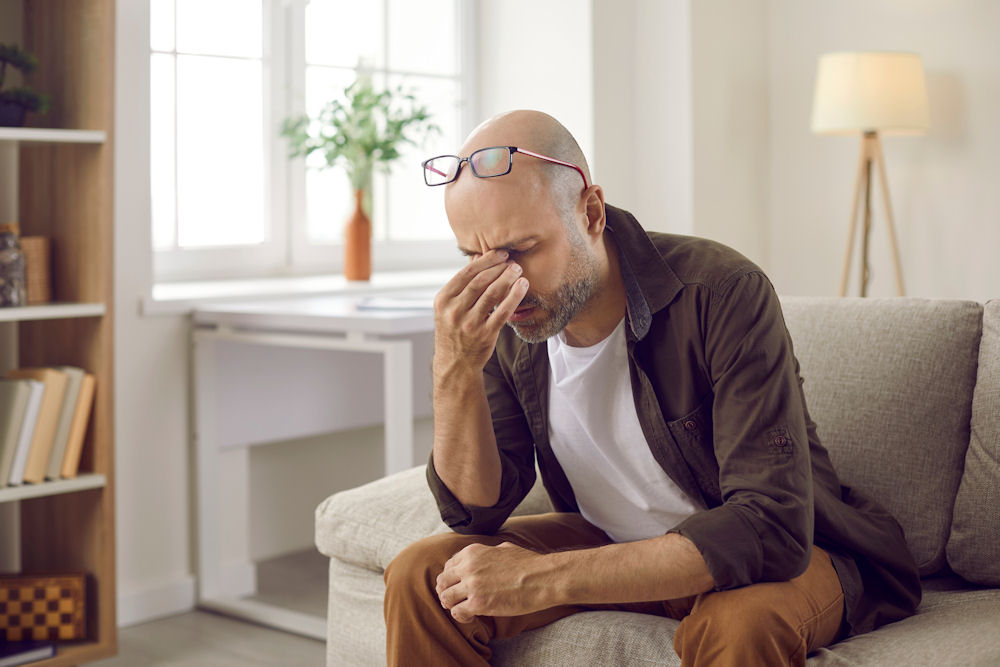 A stressed man sits on a couch, affected by alcohol and cortisol